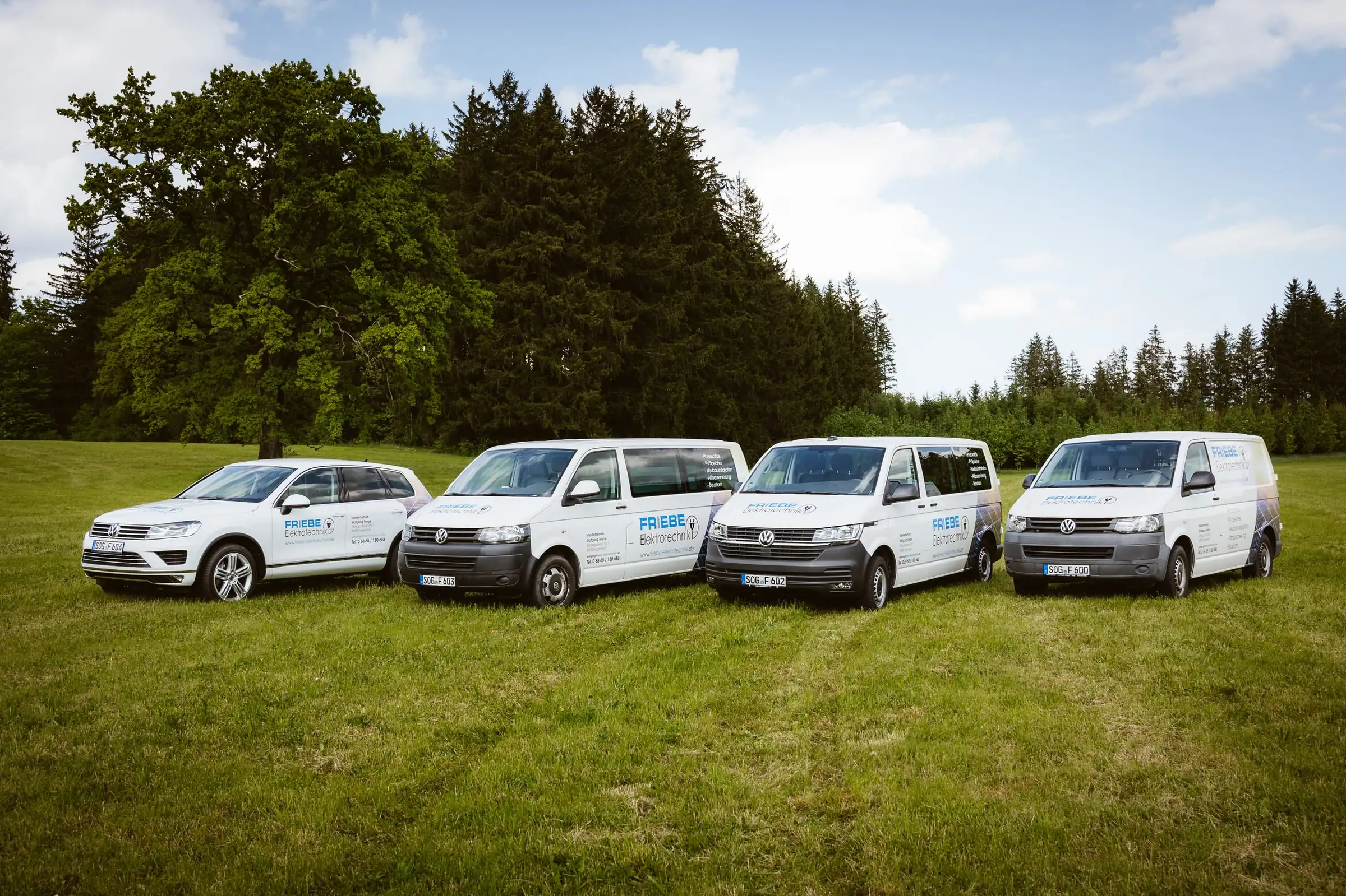 Vier beschriftete Firmenfahrzeuge von Friebe Elektrotechnik auf einer Wiese