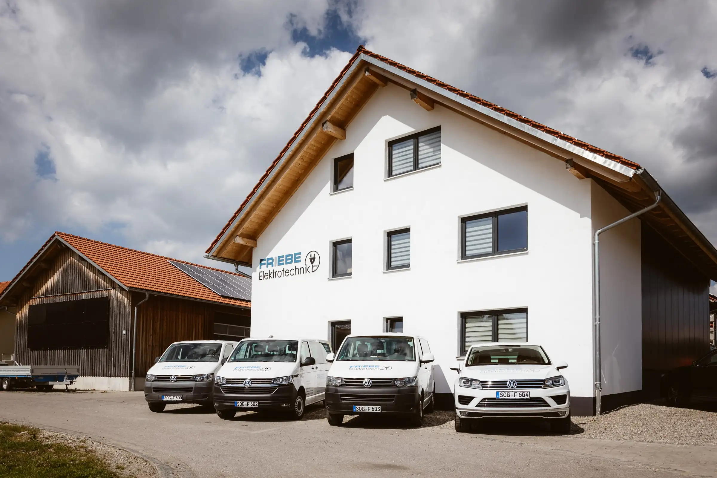 Weißes Gebäude mit Friebe-Elektrotechnik-Schriftzug, davor vier Firmenfahrzeuge
