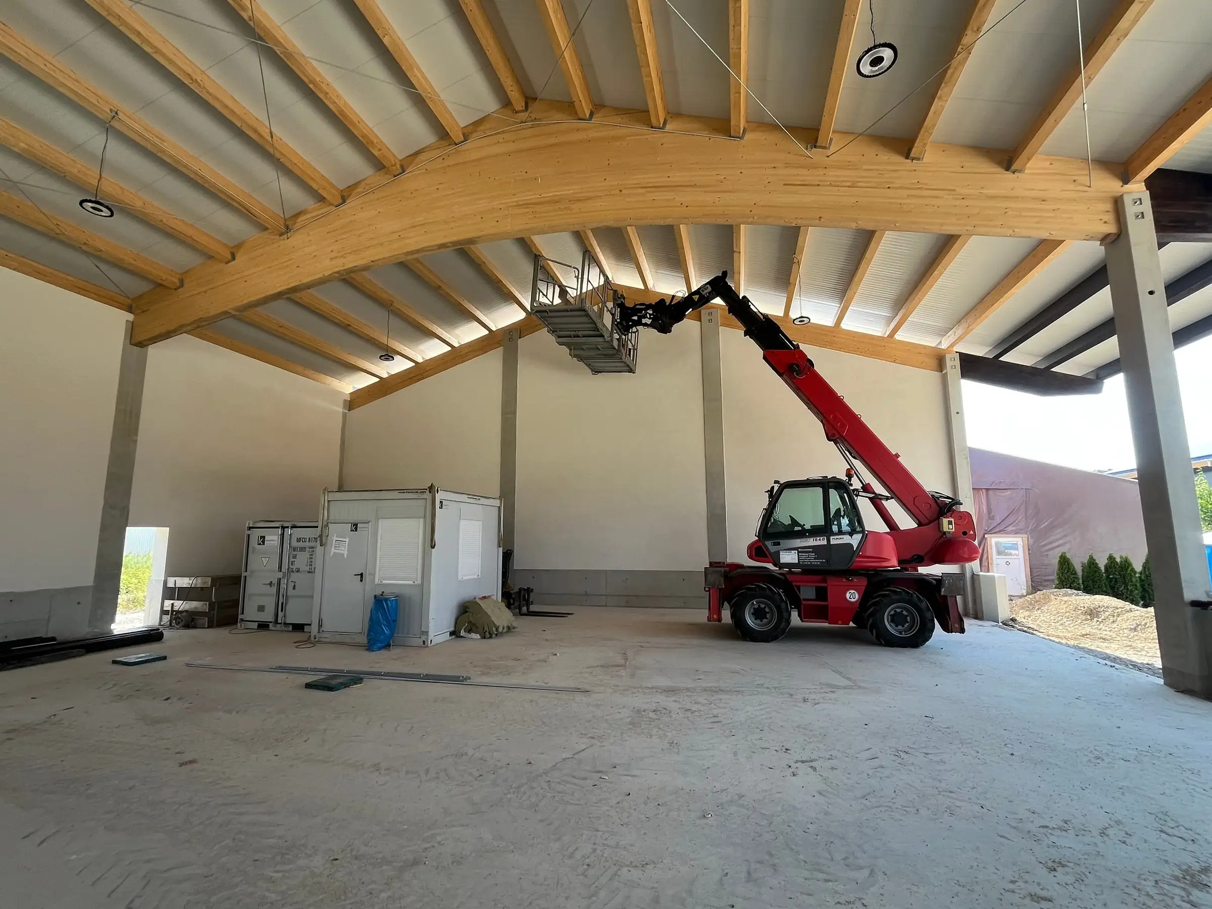 Rohbau einer Halle mit Holzdach, Teleskoplader und Arbeitskorb für die Installation unter der Decke
