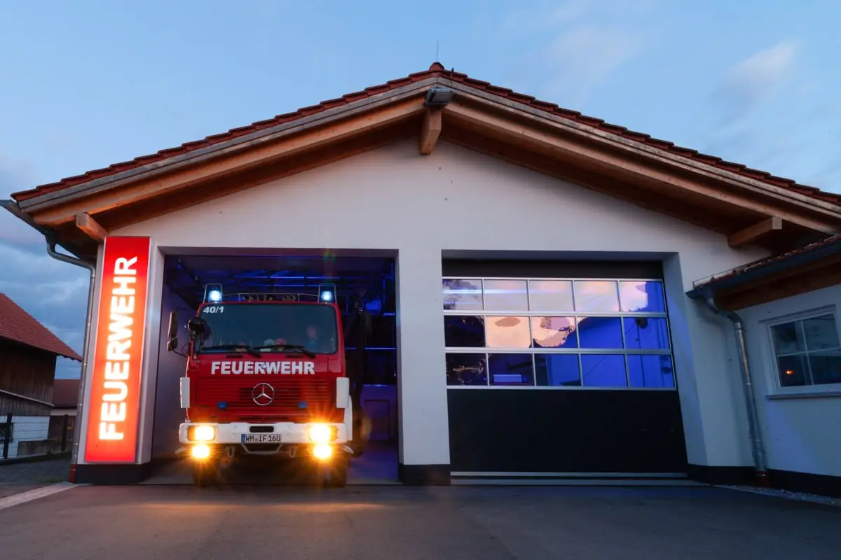 Feuerwehrhaus Ingenried am Abend, Einsatzfahrzeug mit Licht im geöffneten Tor