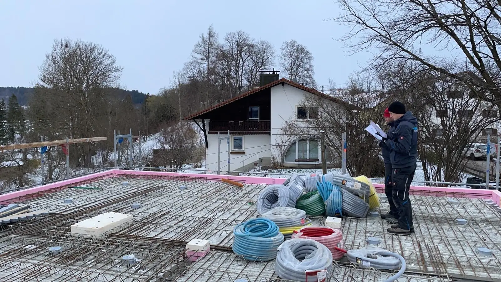 Elektriker prüft auf einer Rohbaudecke die Pläne, daneben Rollen mit Leerrohr für die Installation