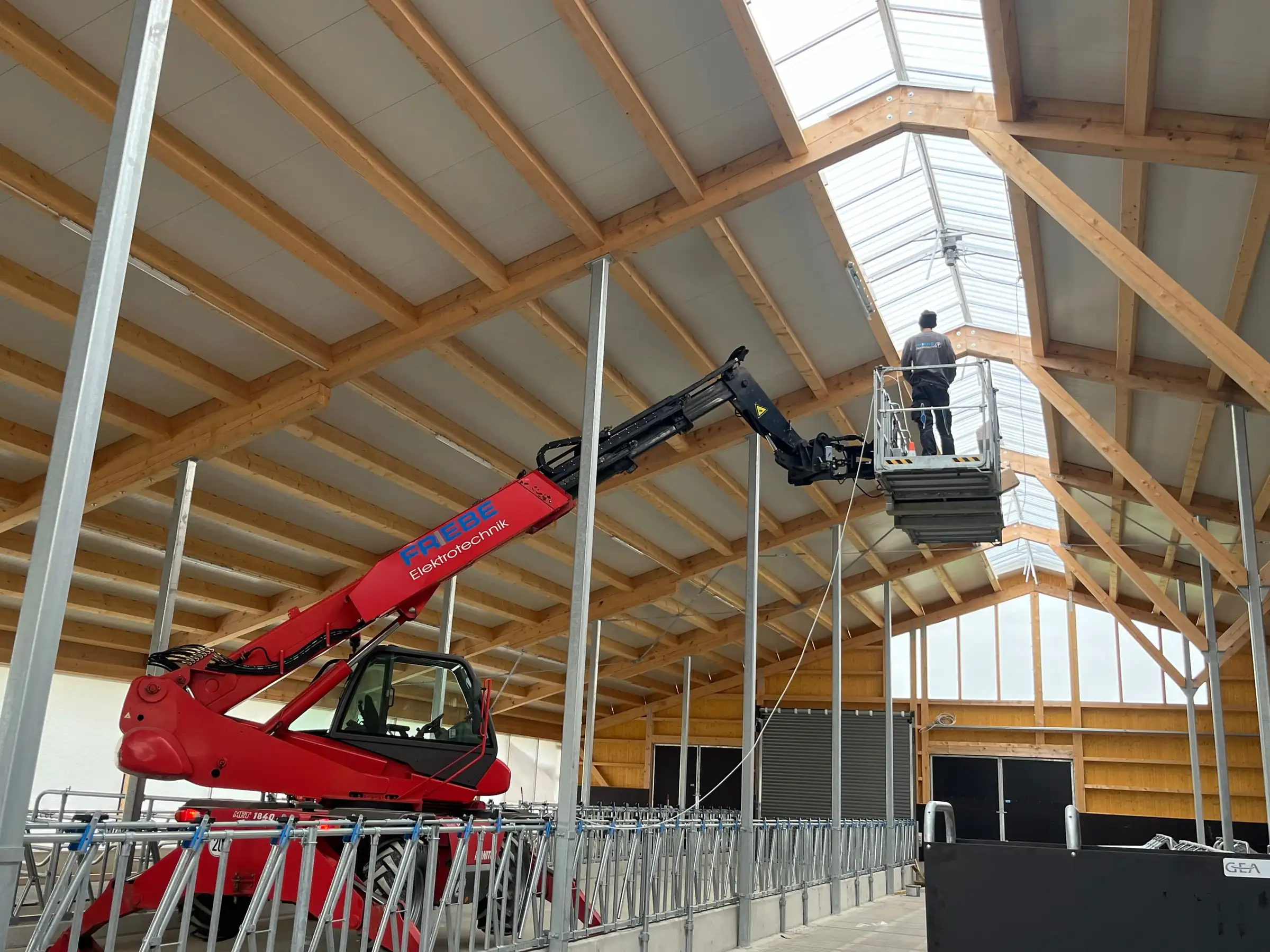 Monteur im Arbeitskorb unter dem Lichtfirst eines neuen Laufstalls
