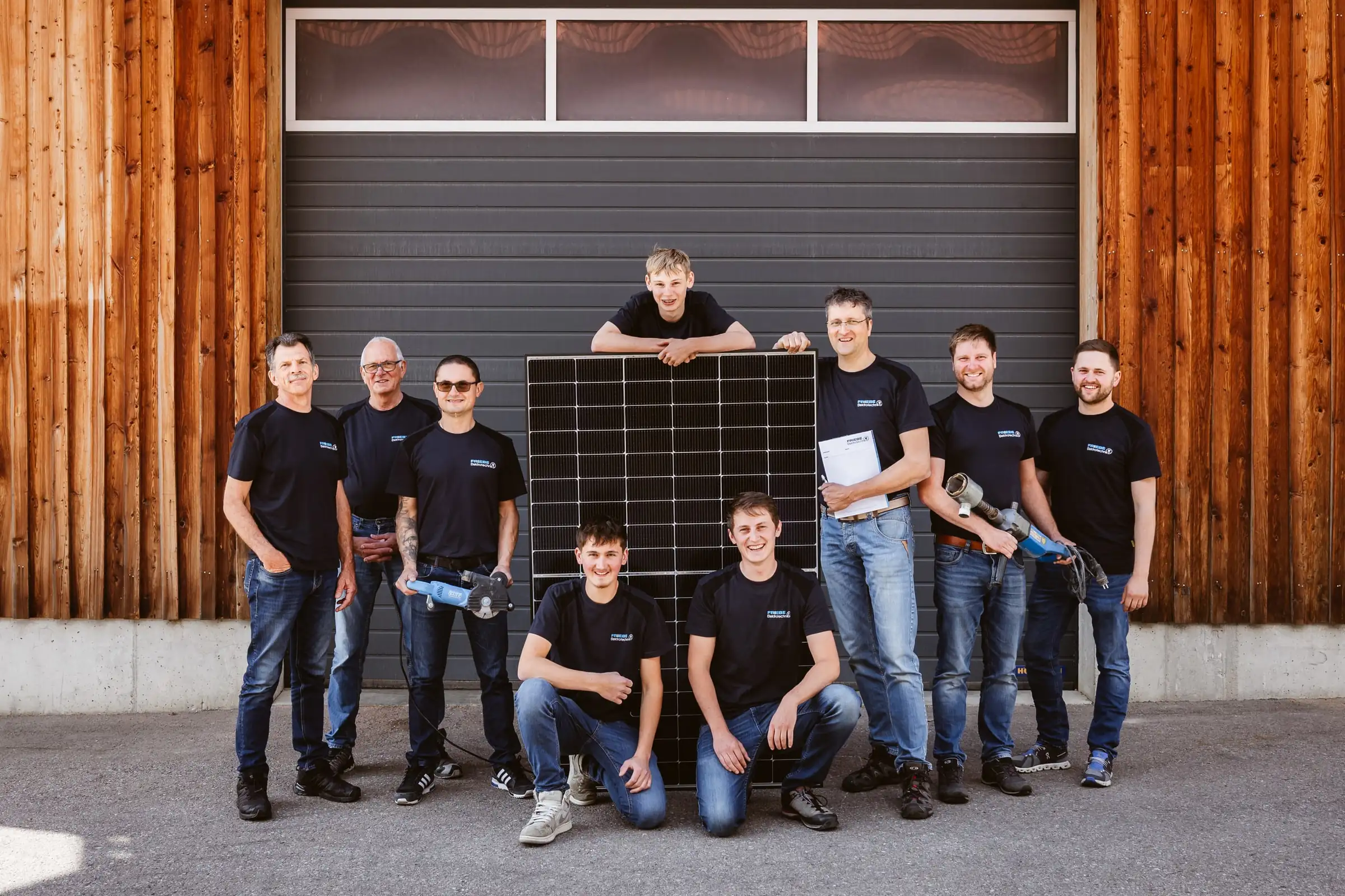 Das Team der Friebe Elektrotechnik mit einem Photovoltaikmodul vor einem Hallentor