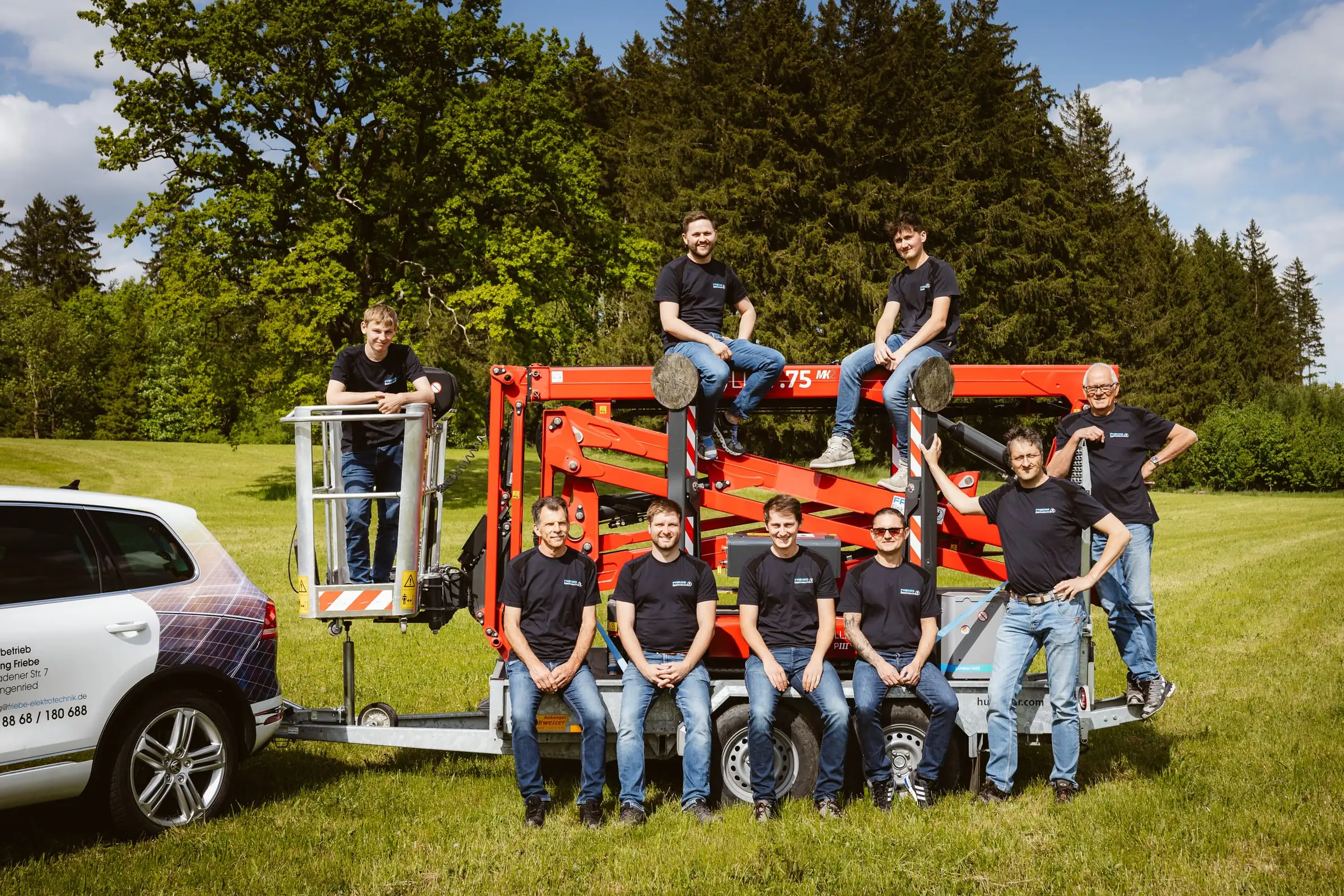 Team von Friebe Elektrotechnik auf und vor einer roten Anhänger-Arbeitsbühne