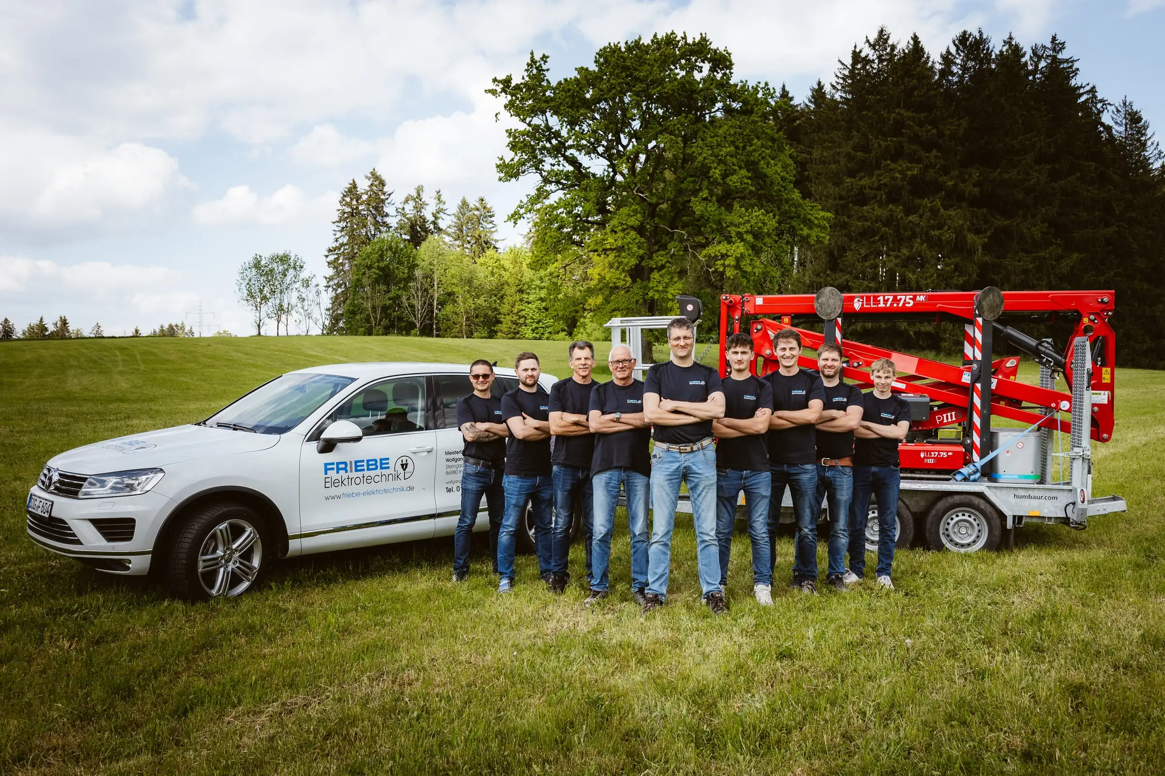 Team von Friebe Elektrotechnik mit Firmenwagen und Arbeitsbühne unter weitem Himmel