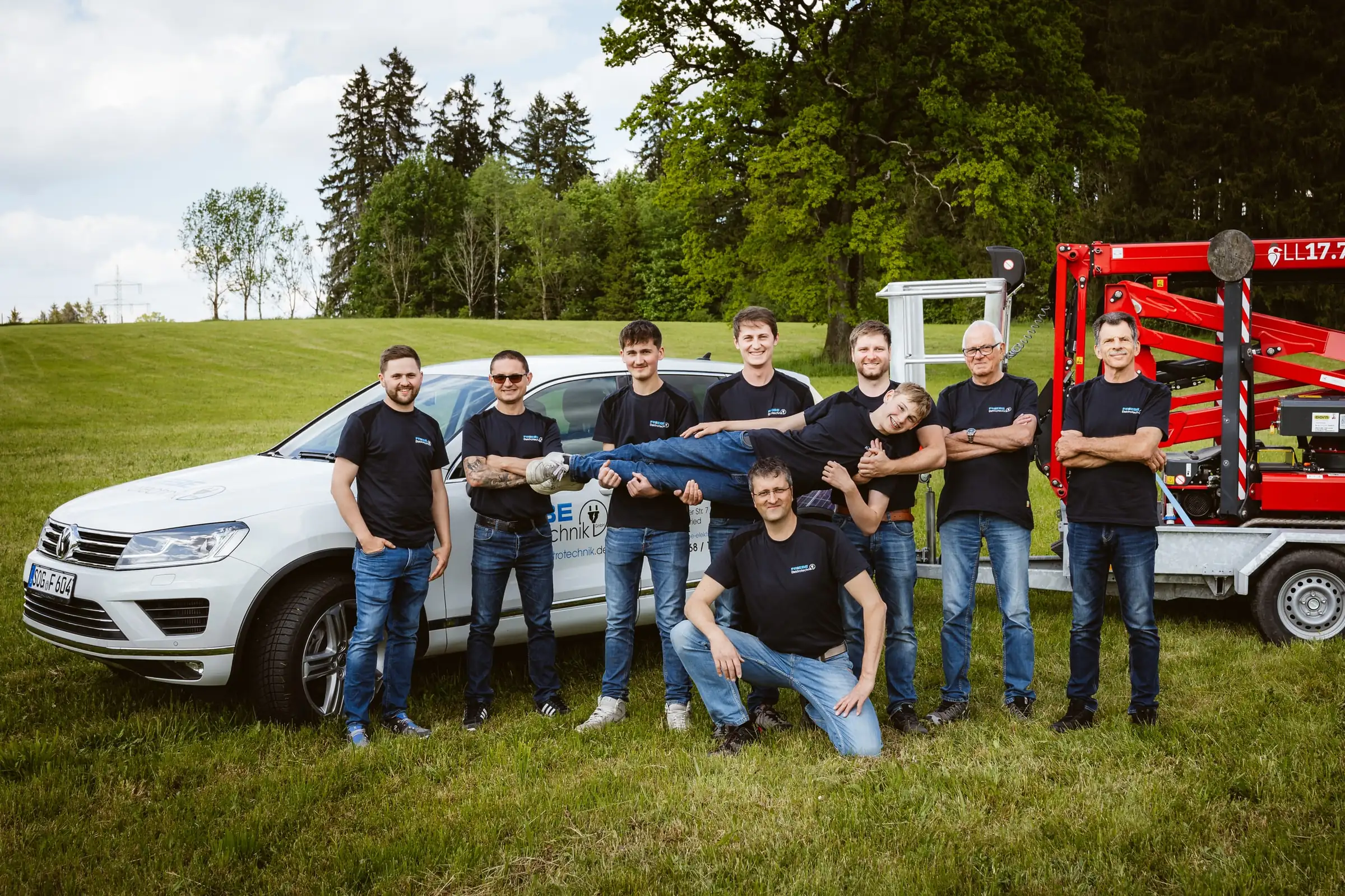 Team von Friebe Elektrotechnik in lockerer Aufstellung vor Firmenwagen und Arbeitsbühne