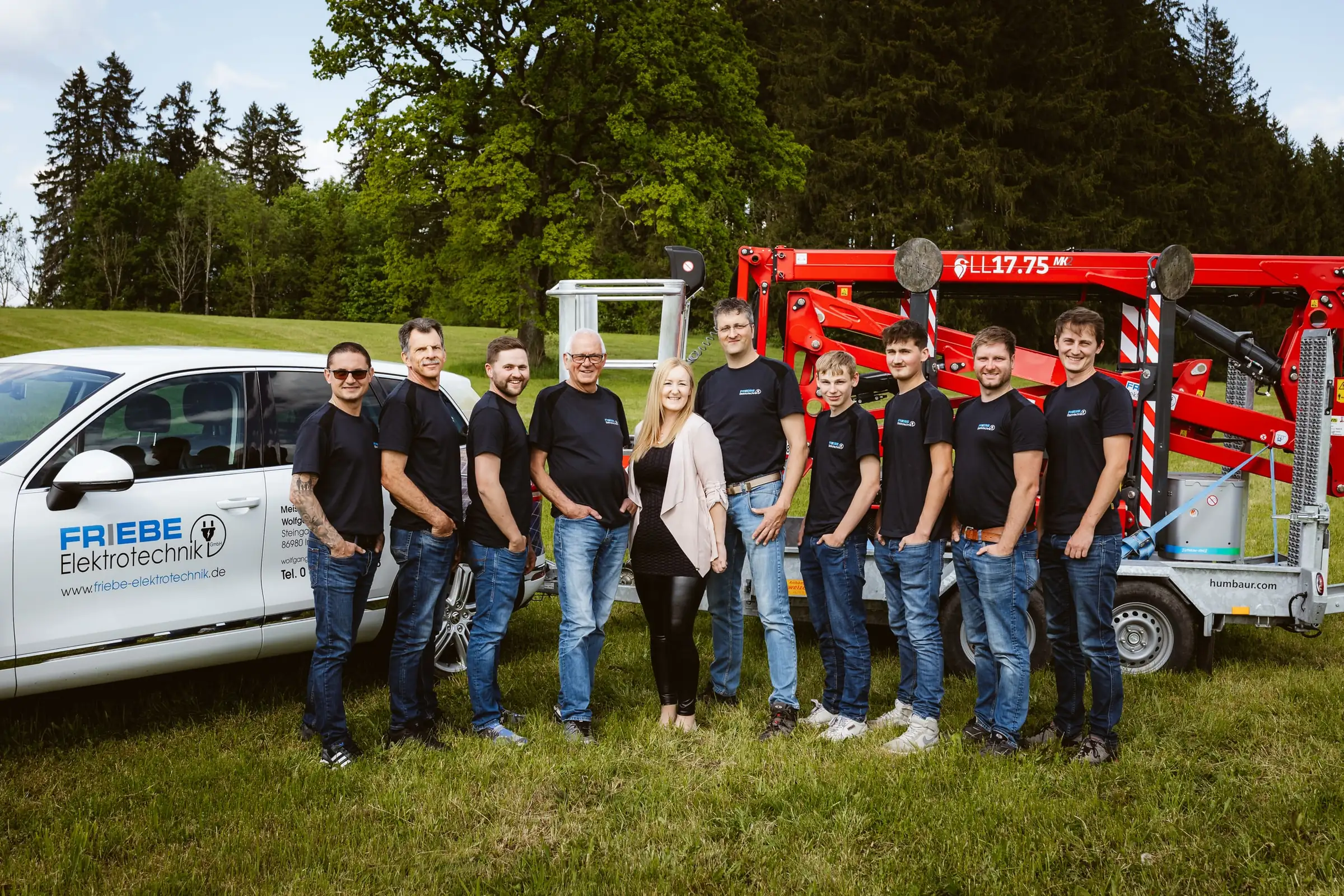 Team von Friebe Elektrotechnik in einer Reihe vor Firmenwagen und Arbeitsbühne
