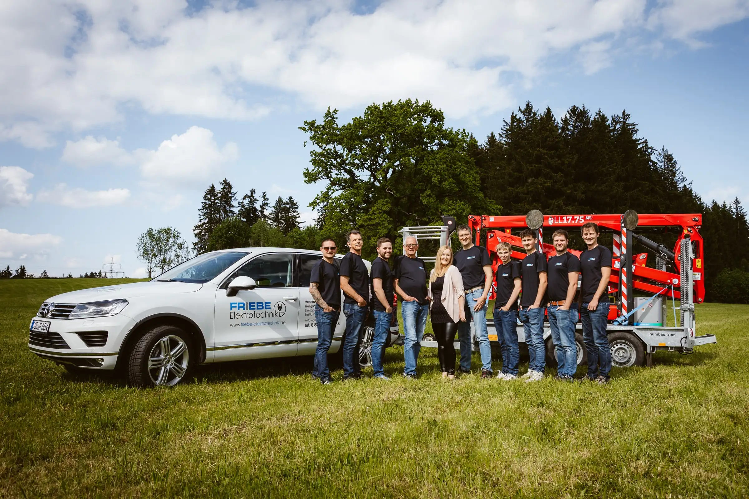 Team von Friebe Elektrotechnik mit Firmenwagen und Arbeitsbühne auf einer Wiese