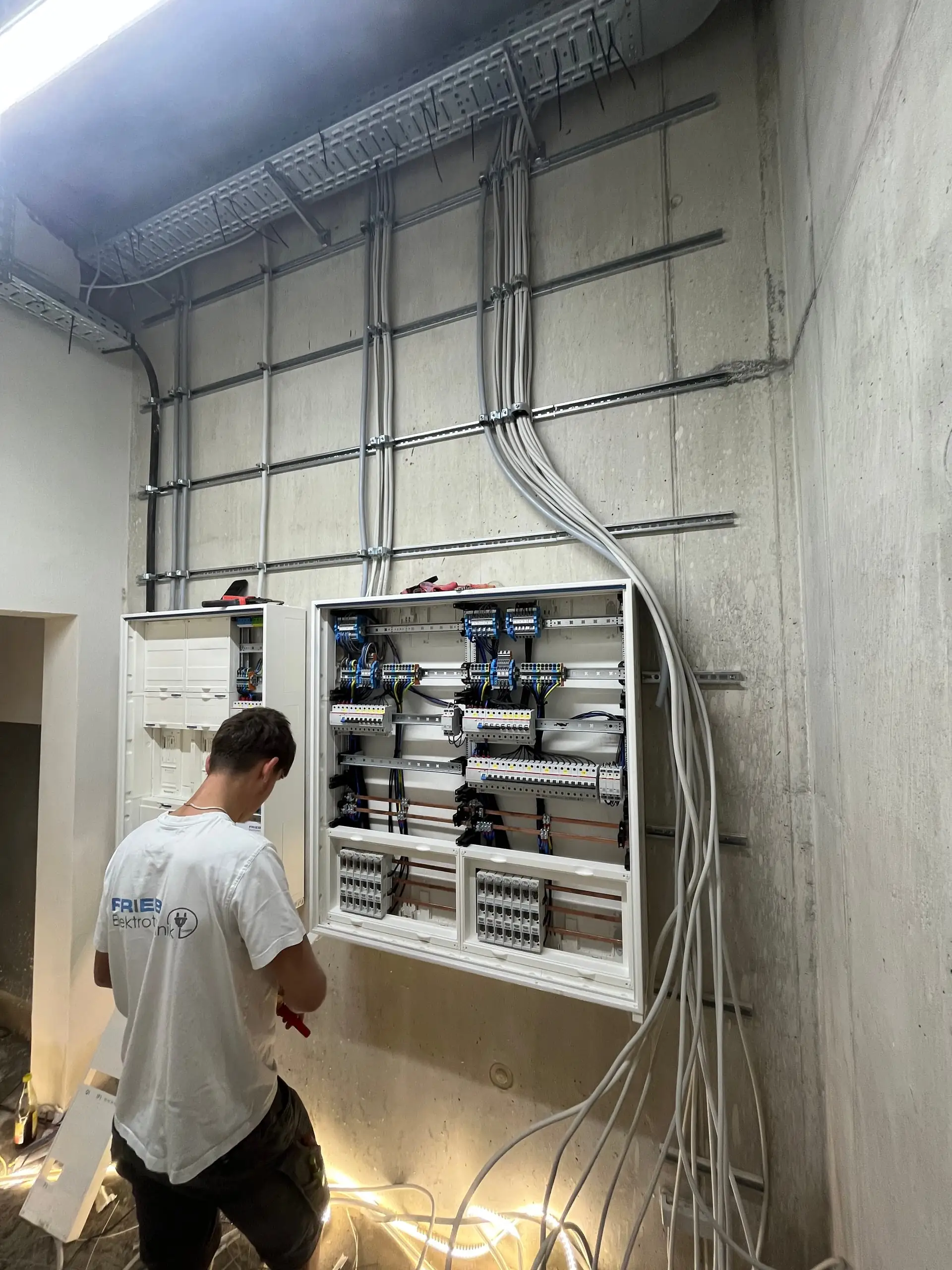 Technikraum mit Kabeltrassen und Verteilung, ein Monteur arbeitet an den Anschlüssen